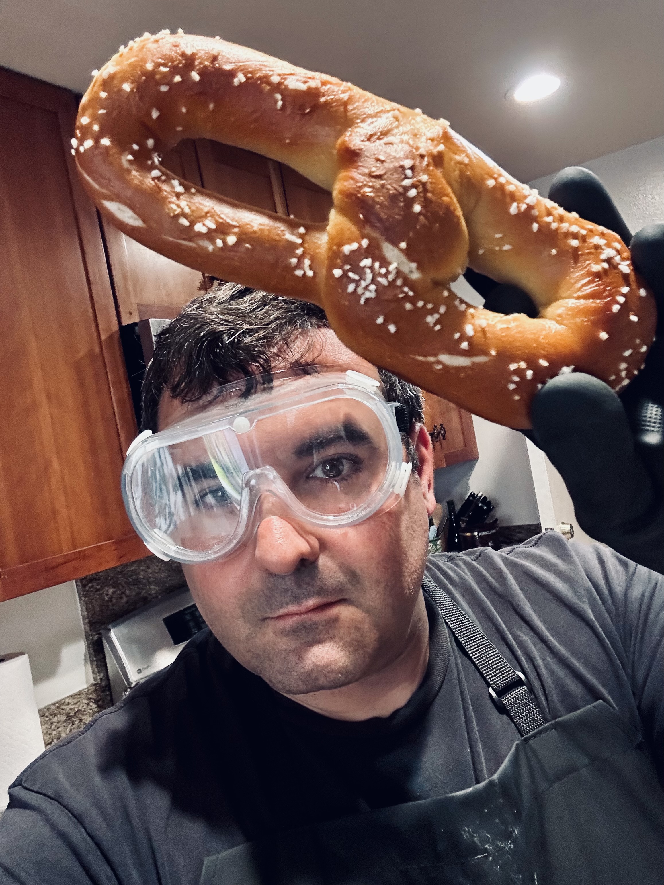 Dave, safety goggles on, holding up a fresh pretzel