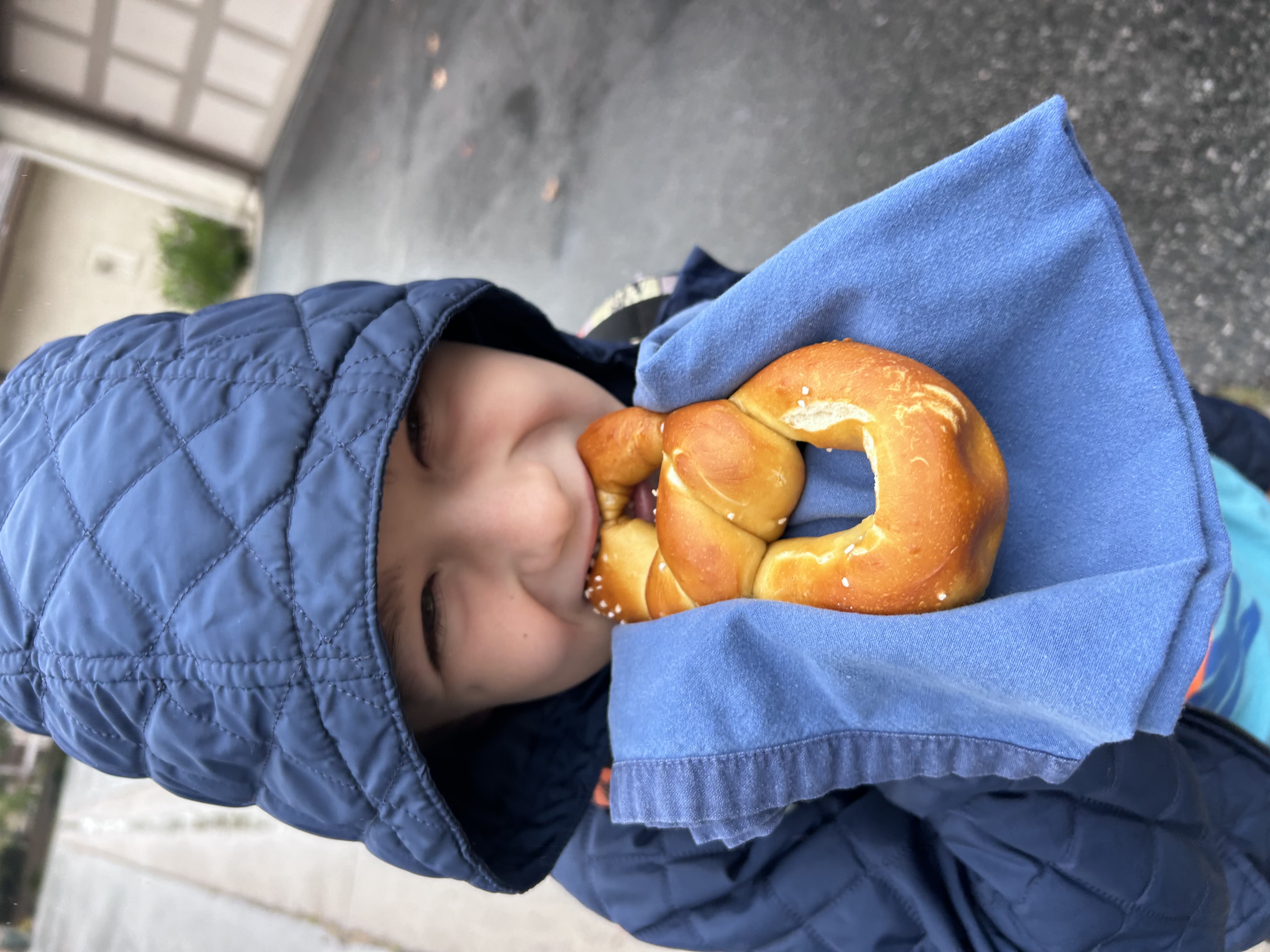 A kid taking a big happy bite out of a fresh pretzel